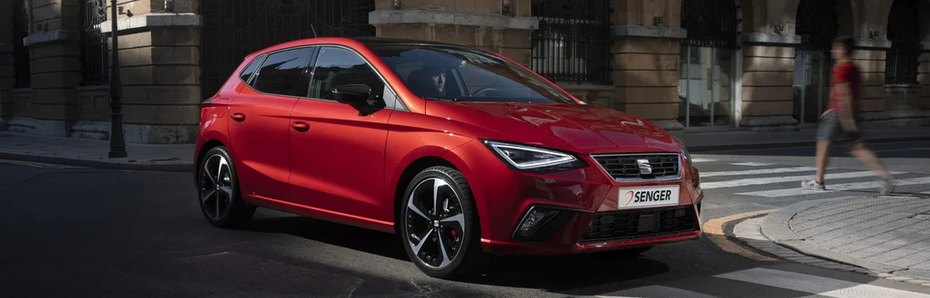 Ein roter SEAT Ibiza fährt über eine asphaltierte Straße durch eine Stadt.