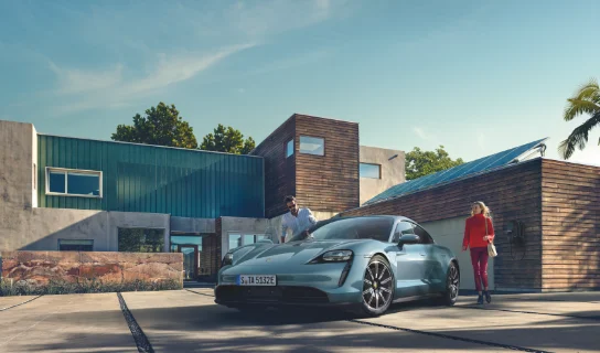 Ein silberner Porsche steht vor einem haus mit Solaranlage, daneben ein Mann und eine Frau.