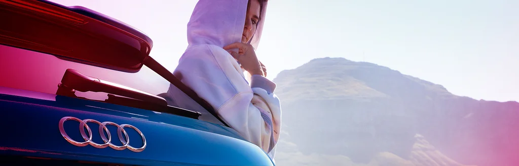 Frau die hinter einem Audi steht und im Hintergrund sieht man einen Berg.