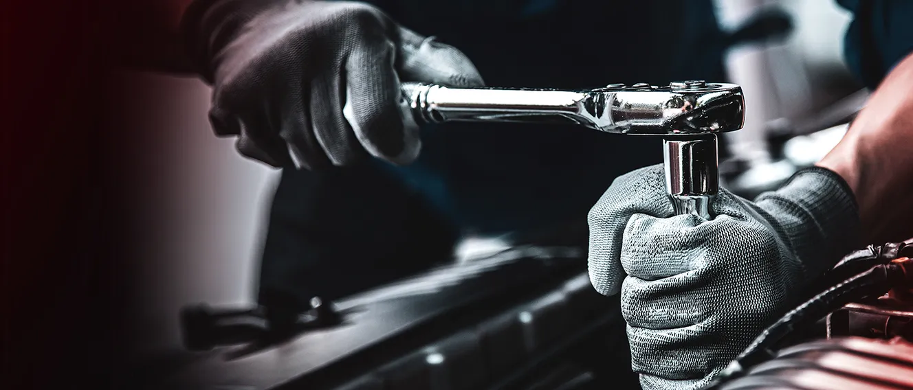 Nahaufnahme der Hände eines Mannes, der an einem Auto mit einem Steckschlüssel arbeitet.