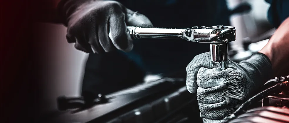 Nahaufnahme der Hände eines Mannes, der an einem Auto mit einem Steckschlüssel arbeitet.