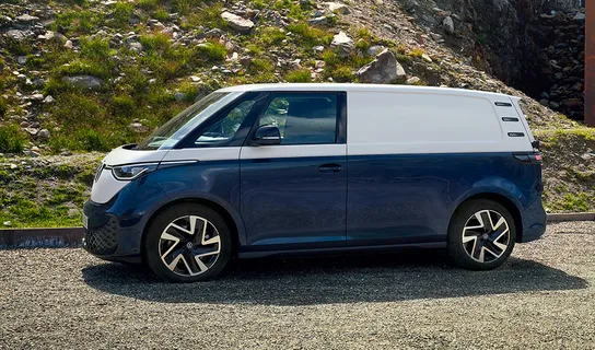 Der vollelektrische VW ID. Buzz Cargo in weiß-blau steht auf einer Schotterstraße.