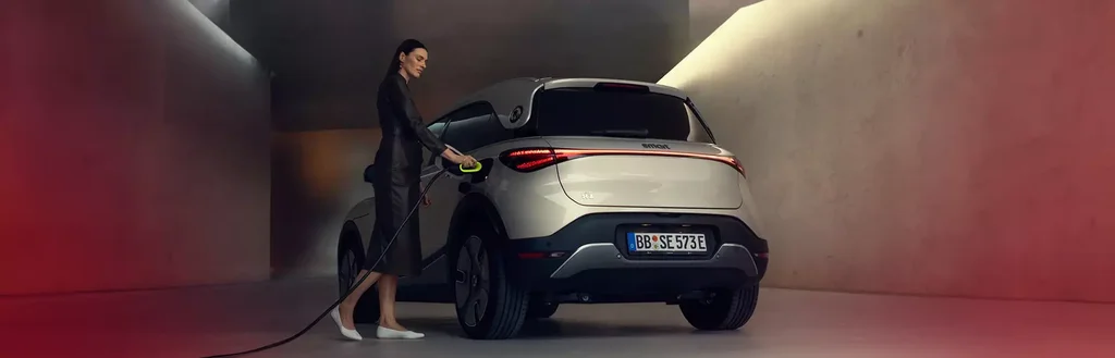 Ein weißer smart #1 wird von einer Frau in einem dunklen Kostüm geladen.